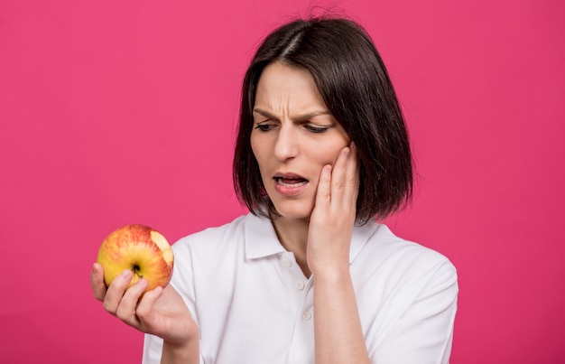 Beautiful young woman bites a big apple and has a toothache