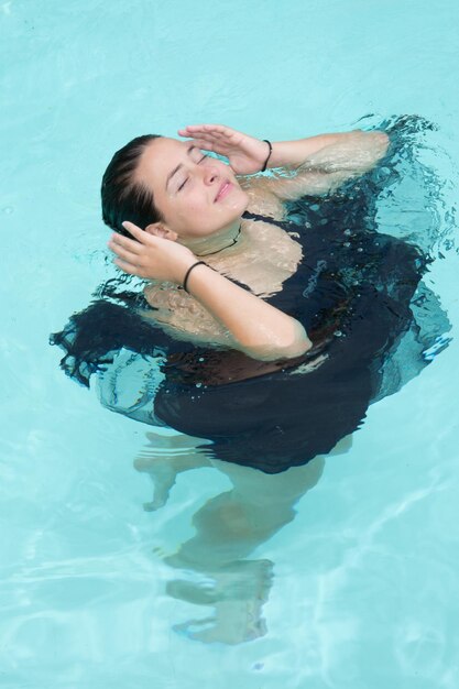 Beautiful young woman in black dress girl swimming in swimming pool