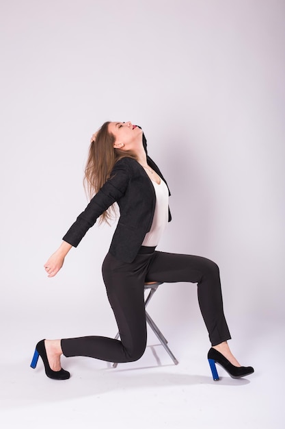 Beautiful young woman in black suit sits on a chair on white background