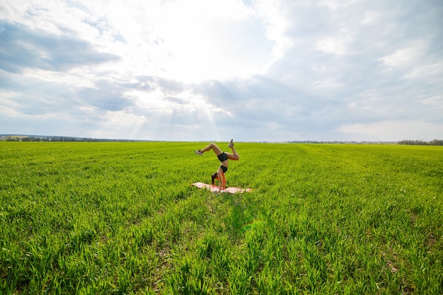 Beautiful young woman in a black top and shorts performs a handstand. A model stands on her hands, doing gymnastic splits against the blue sky. Healthy lifestyle concept