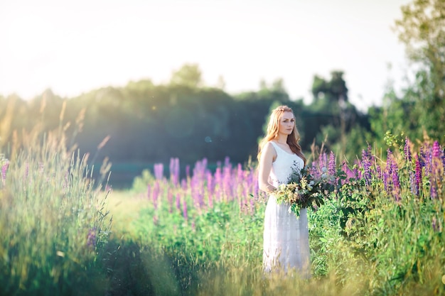 Beautiful young woman over blooming lupines with bunch of flowers in hands