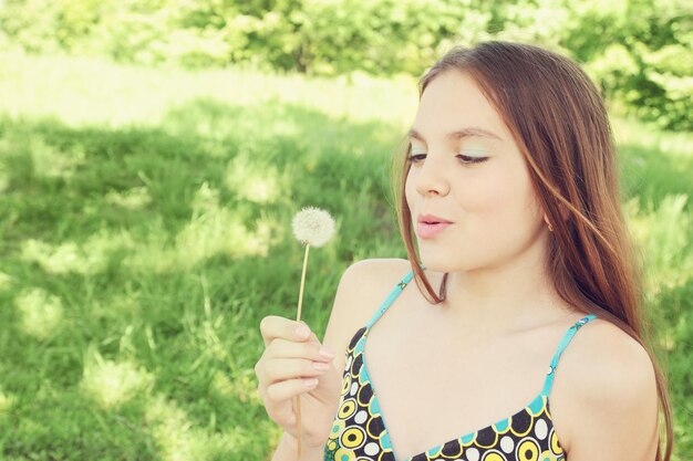 Beautiful young woman blowing on dandelion fluffy