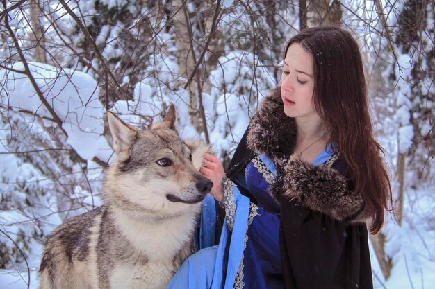 Beautiful young woman in a blue dress communicates with a wolf in a snow-covered forest