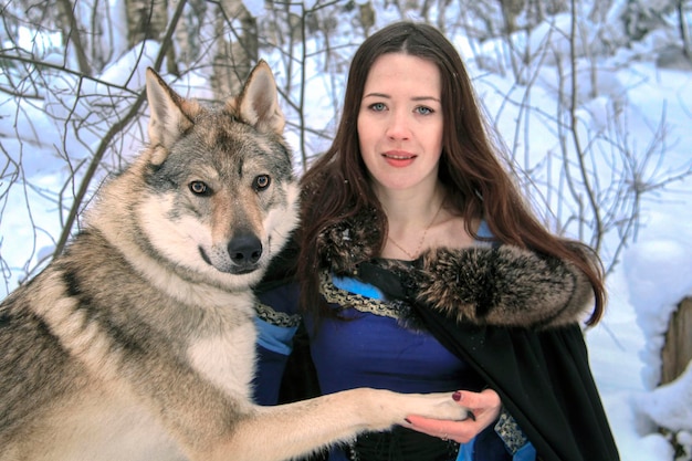 Foto la bella giovane donna in un vestito blu comunica con un lupo in una foresta innevata