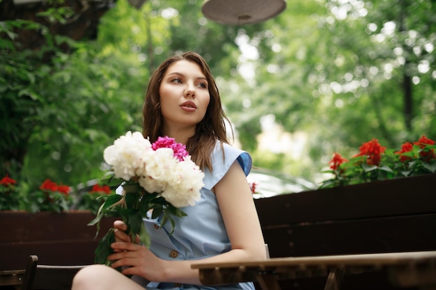 Photo a beautiful young woman in a blue dress with a bouquet of peonies