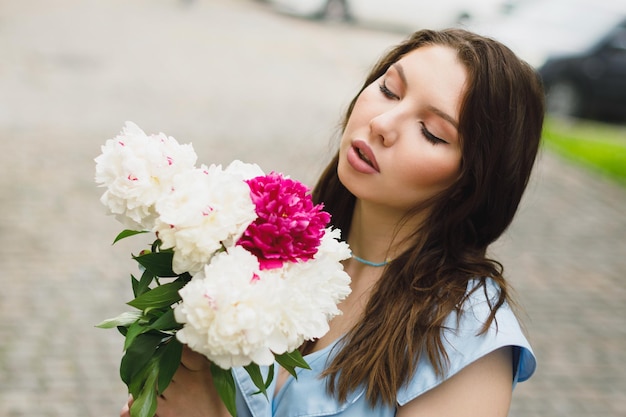 A beautiful young woman in a blue dress with a bouquet of peonies