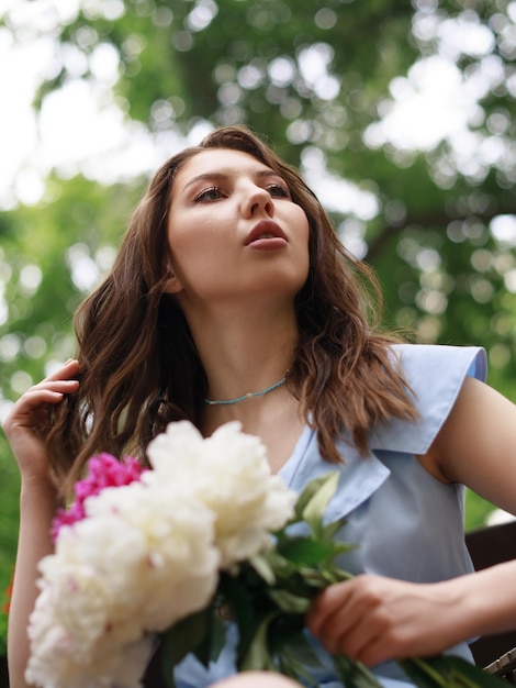 Una bella giovane donna in un vestito blu con un mazzo di peonie