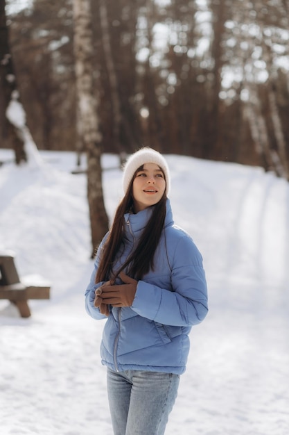 A beautiful young woman in a blue jacket is walking in a winter park