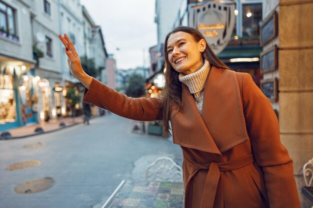 Beautiful young woman in brown coat catching taxi on the street