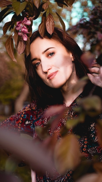Beautiful young woman by branches with burgundy and green leaves