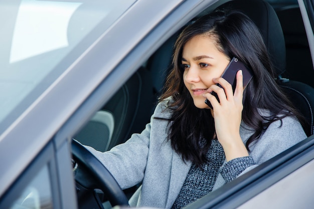 Beautiful young woman in the car smiling and talking on a cell phone.