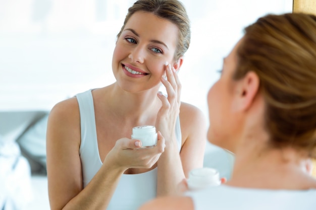 Photo beautiful young woman caring of her skin standing near mirror in the bathroom.