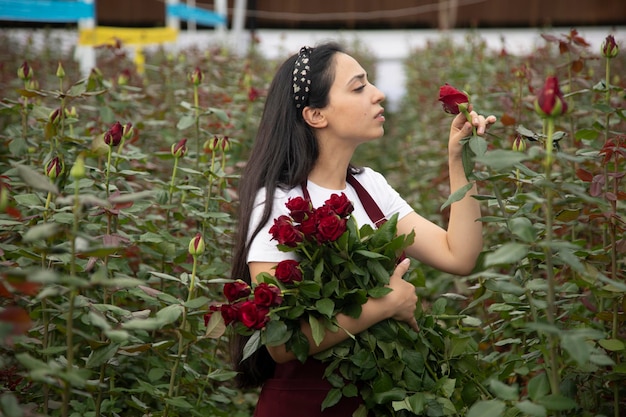 Красивая молодая женщина ухаживает за розами в теплице