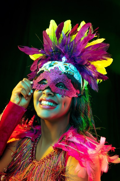 Beautiful young woman in carnival mask and masquerade costume in colorful lights