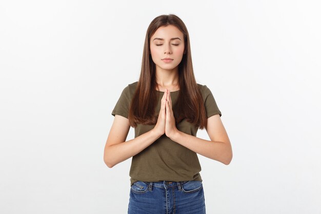 Beautiful young woman in casual clothes holding hands together and praying, isolated on white.