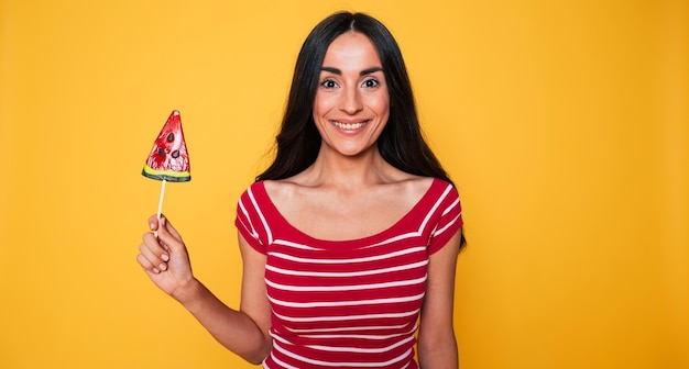 Beautiful young woman in casual clothes with lollipop in hands posing on orange background