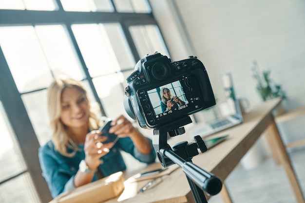 Photo beautiful young woman in casual clothing smiling while working in front of digital camera