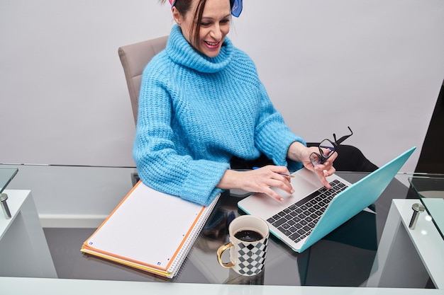 Beautiful young woman in casual clothing using laptop and smiling while working home