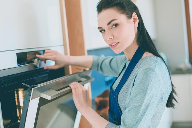 Beautiful young woman checking how her cake is doing in the oven