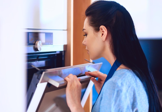 Beautiful young woman checking how her cake is doing in the oven