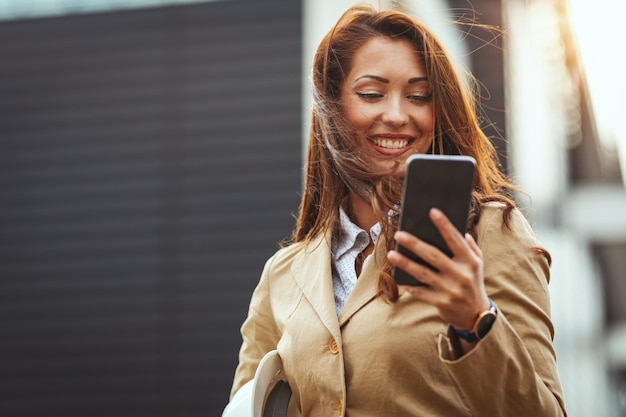 Beautiful young woman checking message on her smartphone on the move against urban city background.