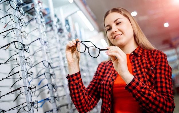 Beautiful young woman choosing new pair of spectacles in opticians store Eyesight correction Optics Ophthalmology