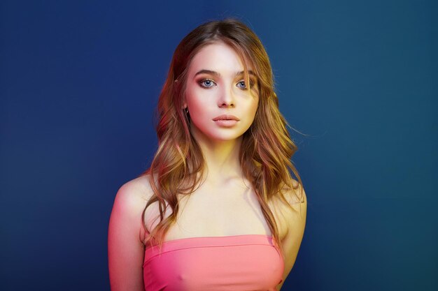 Beautiful young woman in color lights over blue background