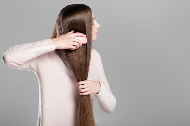 Beautiful young woman combing her smooth long natural hair with hairbrush