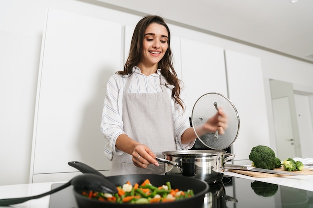 フライパンを使用して、キッチンで健康的な夕食を調理する美しい若い女性