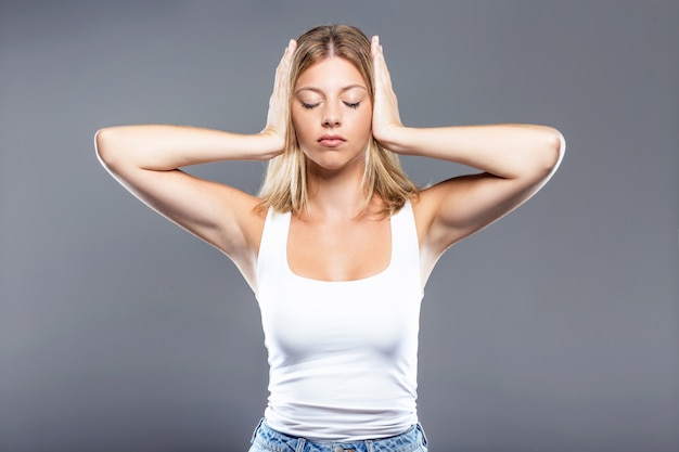 Beautiful young woman covering her ears over gray background.