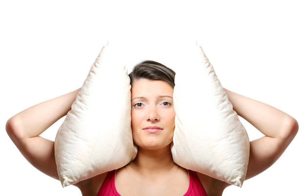 a beautiful young woman covering her ears with a pillow over white background