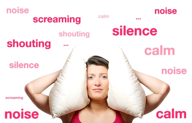 a beautiful young woman covering her ears with a pillow over white background