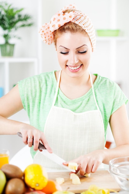 Foto bella giovane donna che taglia mela in una cucina.