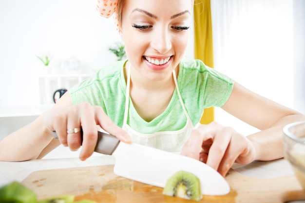 Beautiful young woman cutting kiwi in a kitchen.