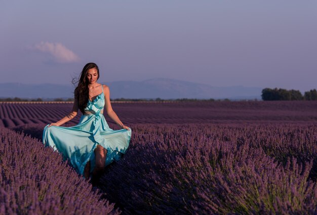 beautiful young woman in cyand dress relaxing and having fun on wind in purple lavander flower field