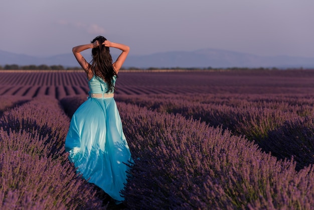 beautiful young woman in cyand dress relaxing and having fun on wind in purple lavander flower field