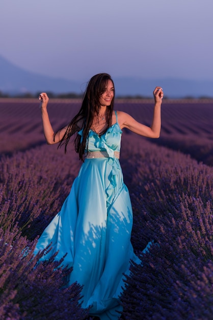 красивая молодая женщина в синем платье расслабляется и веселится на ветру в фиолетовом цветочном поле лаванды