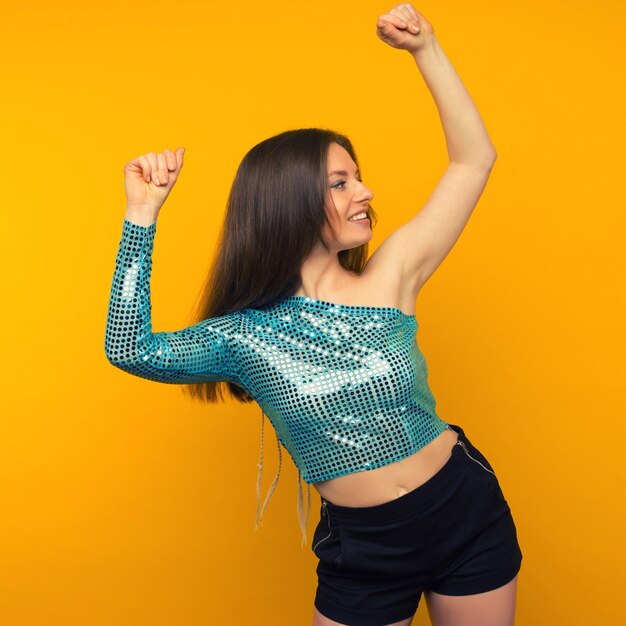 Beautiful young woman dancer in a shiny blue cape posing on a yellow background.