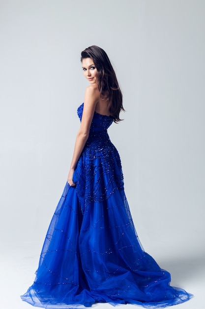 Photo beautiful young woman in a dark blue dress over a light gray wall