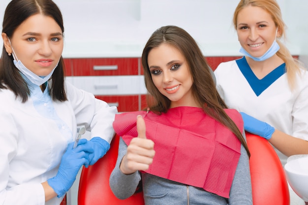 Красивая молодая женщина на приеме у стоматолога показывает палец вверх