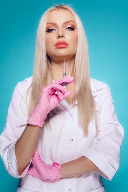 Beautiful young woman doctor beautician in medical uniform holding syringe 