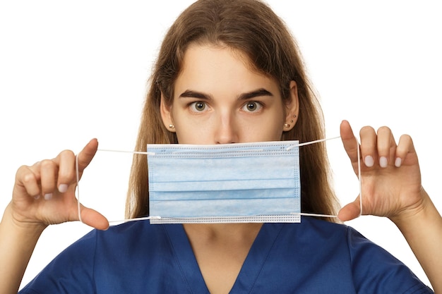 Beautiful young woman doctor surgeon putting on a protective disposable face mask isolated on white background Virus protection concept The modern viral threat of coronavirus