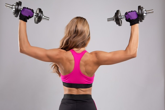 A beautiful young woman does exercises with dumbbells on the back muscles.