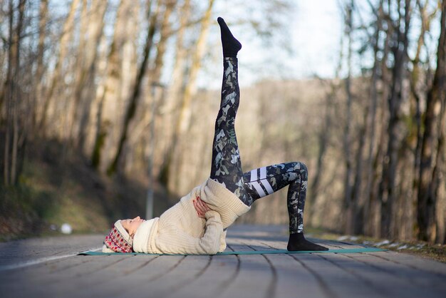 Foto bella giovane donna che fa hatha yoga e medita sul marciapiede nel parco della città