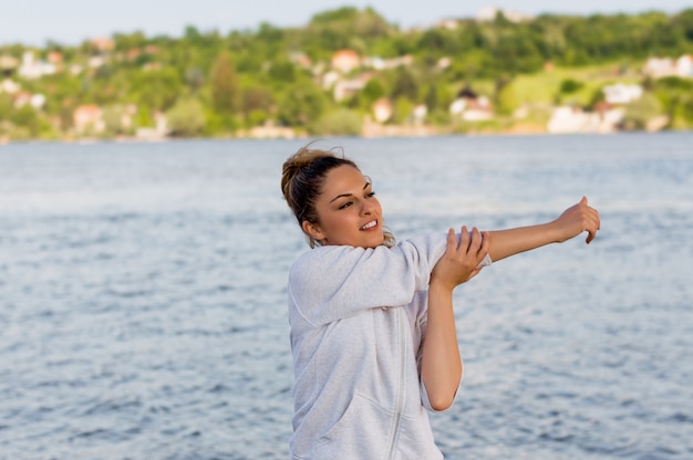 Beautiful young woman doing stretching exercises while standing outdoors 