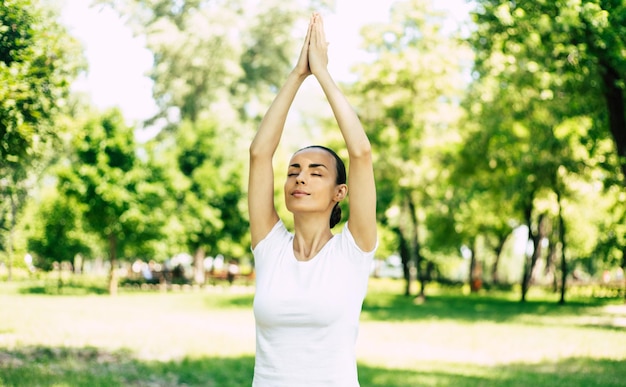 Beautiful young woman doing yoga at park and looking away. Brunette woman enjoying nature during a breathing exercise