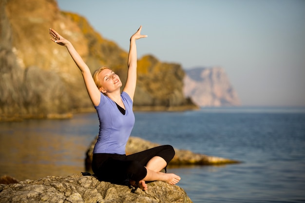 Beautiful young woman doing yoga on a stone