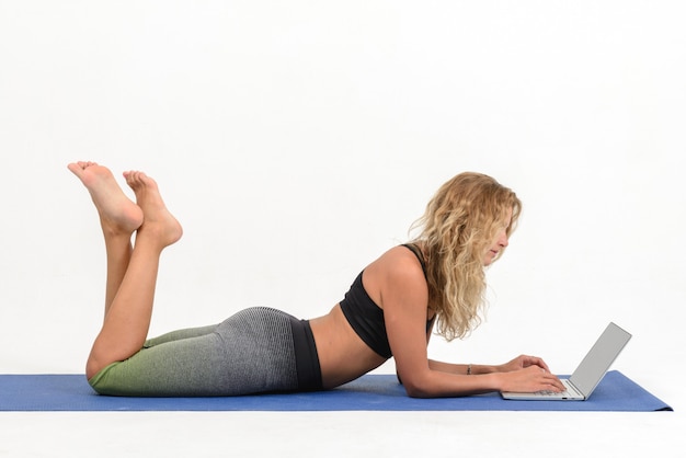 Beautiful young woman doing yoga with laptop on white