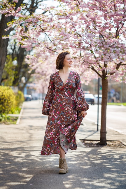 Beautiful young woman in a dress in blooming sakura trees. It's a spring warm sunny day outside