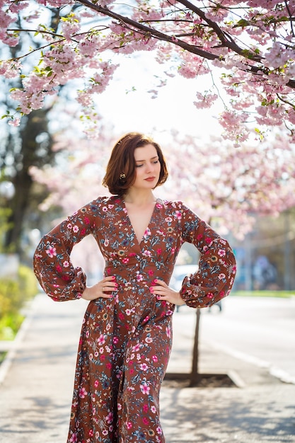 Bella giovane donna in un vestito in alberi di sakura in fiore. fuori è una calda giornata di sole primaverile